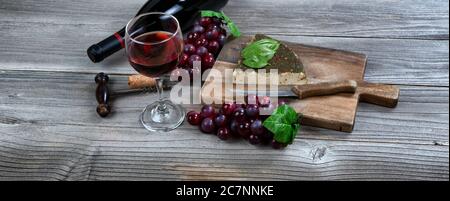 Glass of red wine with fresh cheese wedge plus basil leaves and grapes on rustic wooden table Stock Photo