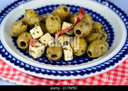 Delicious green olives mixed with cheese cubics and sliced red peppers on a blue patterned plate Stock Photo