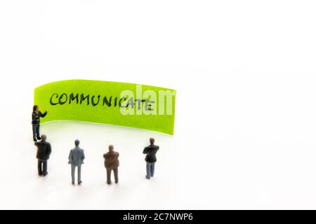 Meeting with miniature figurines posed as business people standing around post-it note with Communicate handwritten message in background, minimalist Stock Photo