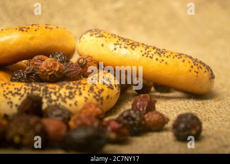 Small bagels and dried rosehip fruit scattered on a homespun cloth with a rough texture. Close up Stock Photo