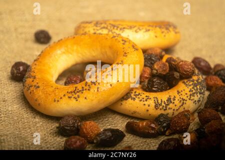 Small bagels and dried rosehip fruit scattered on a homespun cloth with a rough texture. Close up Stock Photo