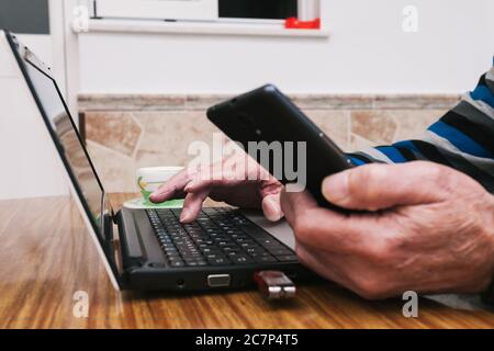Closeup shot of a male hand using a laptop and a cellular phone Stock Photo