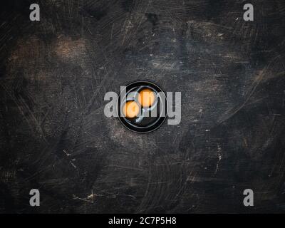 Two yolks of quail eggs in black bowl on wooden background. Stock Photo