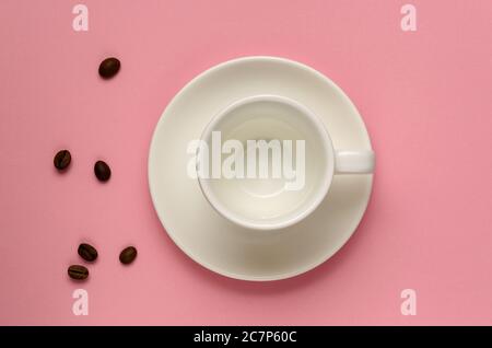 Empty clean white coffee cup on saucer and some coffee beans on millennial pink background. Minimal style. Template for feminine blog, social media Stock Photo
