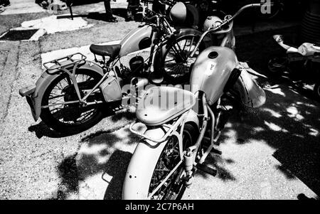 Grayscale shot of retro motorbikes parked close to the shadow cast from the trees Stock Photo