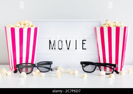 cinema concept - red striped boxes with popcorn, 3d glasses and light box with movie word Stock Photo