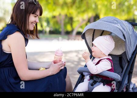 happy mother and cute baby girl eating banana in summer park Stock Photo