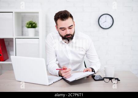 portrait of handsome bearded businessman doing paperwork in modern office Stock Photo