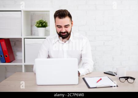 portrait of cheerful bearded businessman using laptop in modern office Stock Photo