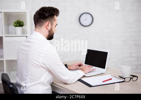 back view of young handsome businessman using laptop in office Stock Photo