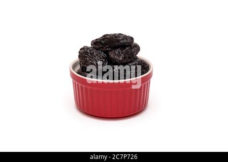 Prunes or dried plums in red ceramic bowl on white background. Natural healthy sweets concept. Closeup. Copy space Stock Photo