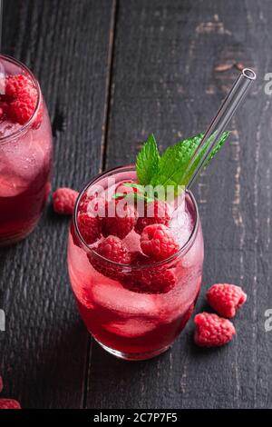 Fresh ice cold berry juice drink with mint, summer raspberry lemonade in two glass with straws on dark wooden background, angle view Stock Photo