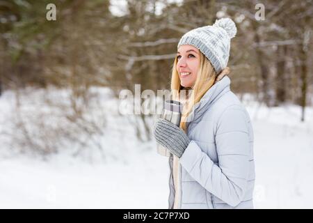 portrait of young blond woman in winter park or forest with thermo cup of coffee Stock Photo