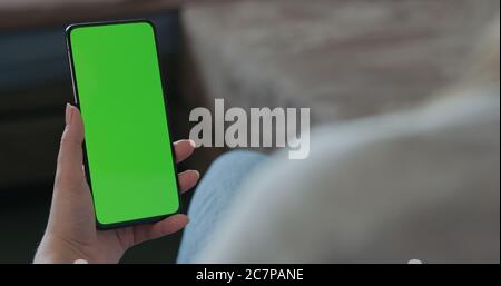 young woman sitting in a chair with smartphone with green screen Stock Photo