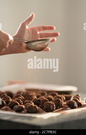 young woman sprinke truffles candy with cocoa powder on kitchen Stock Photo