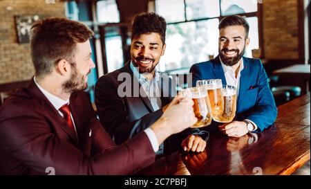 Cheerful old friends having fun and drinking beer at bar counter in pub. Stock Photo