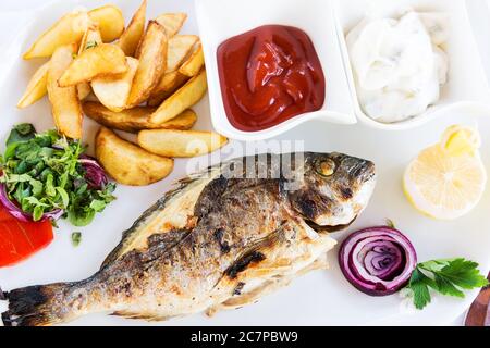 Fried fish dorado with potatoes chips, fresh herbs and lemon Stock Photo