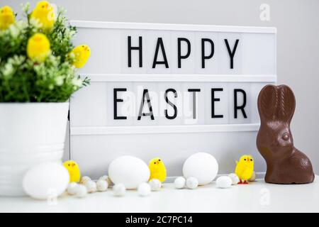 Close up of vintage lightbox with happy Easter greetings, chocolate bunny, Easter eggs and decorations on the table Stock Photo