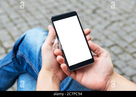 Man uses his Mobile Phone outdoor, close up. Image of young man with mobile smart phone sitting on the bench. Stock Photo