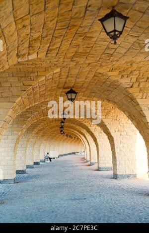 Old architectural perspective from arched brick corridor with arches and columns in Arabic style with old-fashioned lamps on the ceiling. Stock Photo