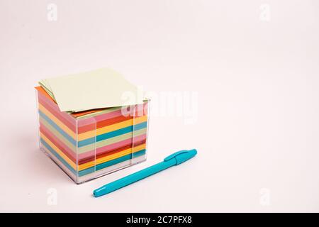 Closeup shot of a box with colorful papers and a blue pen isolated on a light-colored background Stock Photo