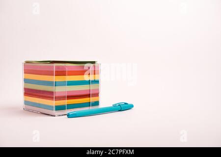 Closeup shot of a box with colorful papers and a blue pen isolated on a light-colored background Stock Photo