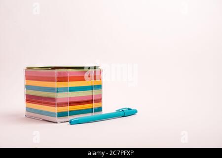 Closeup shot of a box with colorful papers and a blue pen isolated on a light-colored background Stock Photo