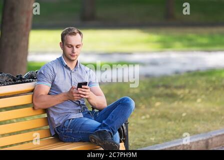 Young man sitting in the park and using a smart phone Stock Photo