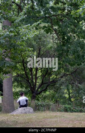 A woman sits alone on a rock surrounded by nature. Surprisingly, this is in New York City. Stock Photo