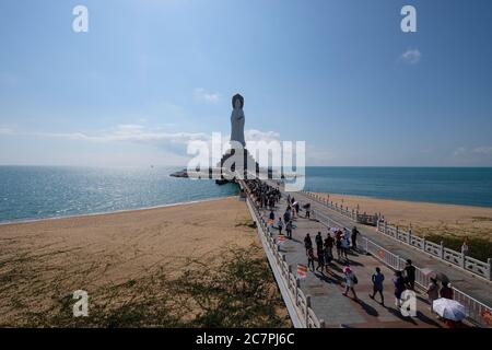 tourists walk along bridge to offer incense to giant three-sided Nanshan Guanyin Holy Statue during Spring Festival.Big Goddess of Mercy on the sea Stock Photo