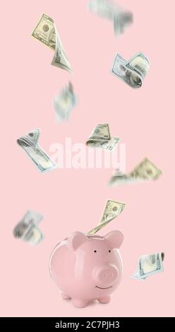 Dollar banknotes falling into pink piggy bank with glasses on white ...