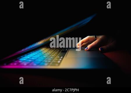 Closeup shot of a woman using a half-opened laptop with colorful lights in a dark setting Stock Photo