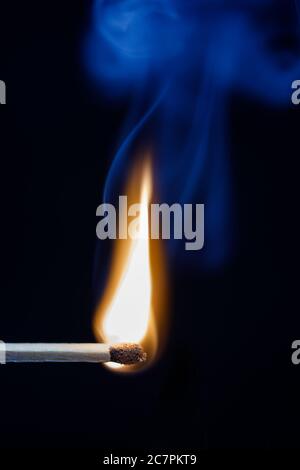 Just lit matchstick with blue smoke rising in the air against a black background Stock Photo