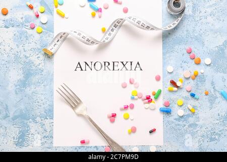 Paper sheet with text ANOREXIA, measuring tape, fork and pills on color background Stock Photo