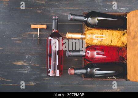 Box with bottles of wine and corkscrew on dark wooden background Stock Photo