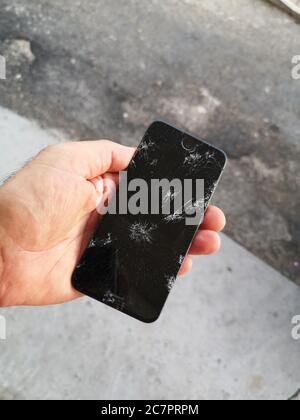 Shallow focus shot of a male holding a smartphone with a cracked screen Stock Photo