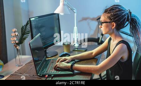 Modern young female programmer is writing program code on a laptop at home. Remote work in the IT profession. The concept of software development. Stock Photo