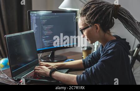 Modern young female programmer is writing program code on a laptop at home. Remote work in the IT profession. The concept of software development. Stock Photo
