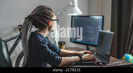 Modern young female programmer is writing program code on a laptop at home. Remote work in the IT profession. The concept of software development. Stock Photo