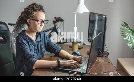 Modern young female programmer is writing program code on a laptop at home. Remote work in the IT profession. The concept of software development. Stock Photo