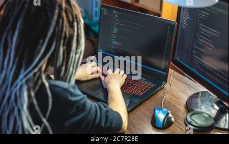 Modern young female programmer is writing program code on a laptop at home. Remote work in the IT profession. The concept of software development. Stock Photo