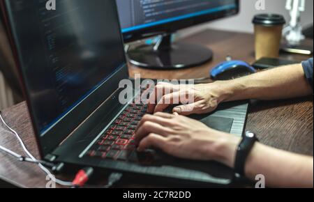 Programmer is writing program code on a laptop at home. Remote work in the IT profession. The concept of software development. Stock Photo