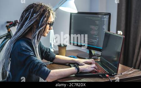 Modern young female programmer is writing program code on a laptop at home. Remote work in the IT profession. The concept of software development. Stock Photo