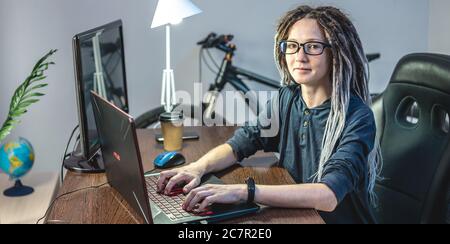 Modern young female programmer is writing program code on a laptop at home. Remote work in the IT profession. The concept of software development. Stock Photo