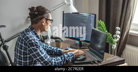 Male programmer is writing program code on a laptop at home. Remote work in the IT profession. The concept of software development. Stock Photo