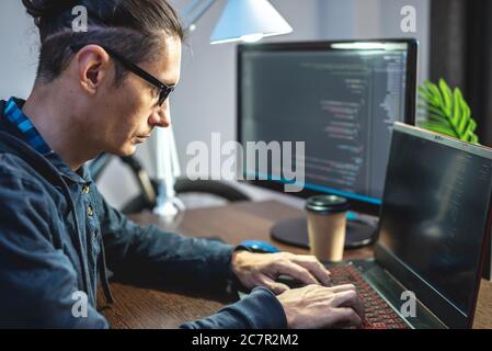 Male programmer is writing program code on a laptop at home. Remote work in the IT profession. The concept of software development. Stock Photo