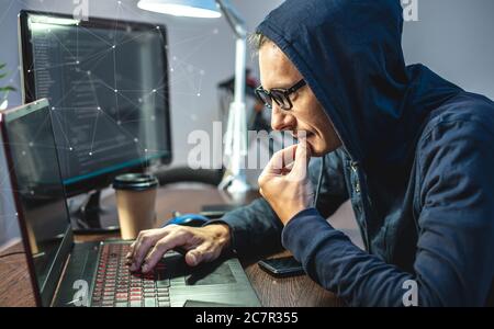Man hacker in a hood are programming virus code on a laptop. The concept of Internet fraud and personal data hacking Stock Photo