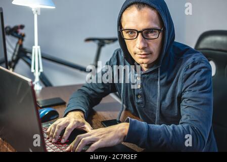 Man hacker in the hood is programming virus code at the keyboard for the laptop. The concept of Internet fraud and personal data hacking Stock Photo