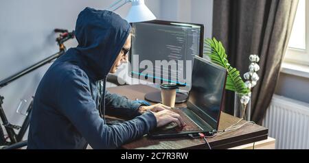 Man hacker in the hood is programming virus code at the keyboard for the laptop. The concept of Internet fraud and personal data hacking Stock Photo