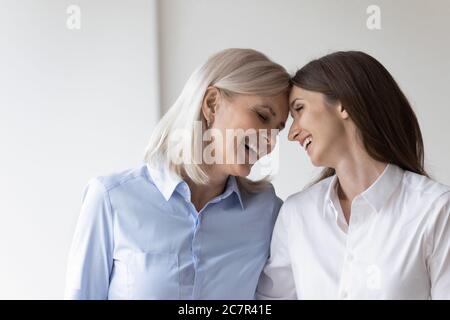 Cheerful elderly mother touch foreheads adult daughter laughing enjoy moment Stock Photo